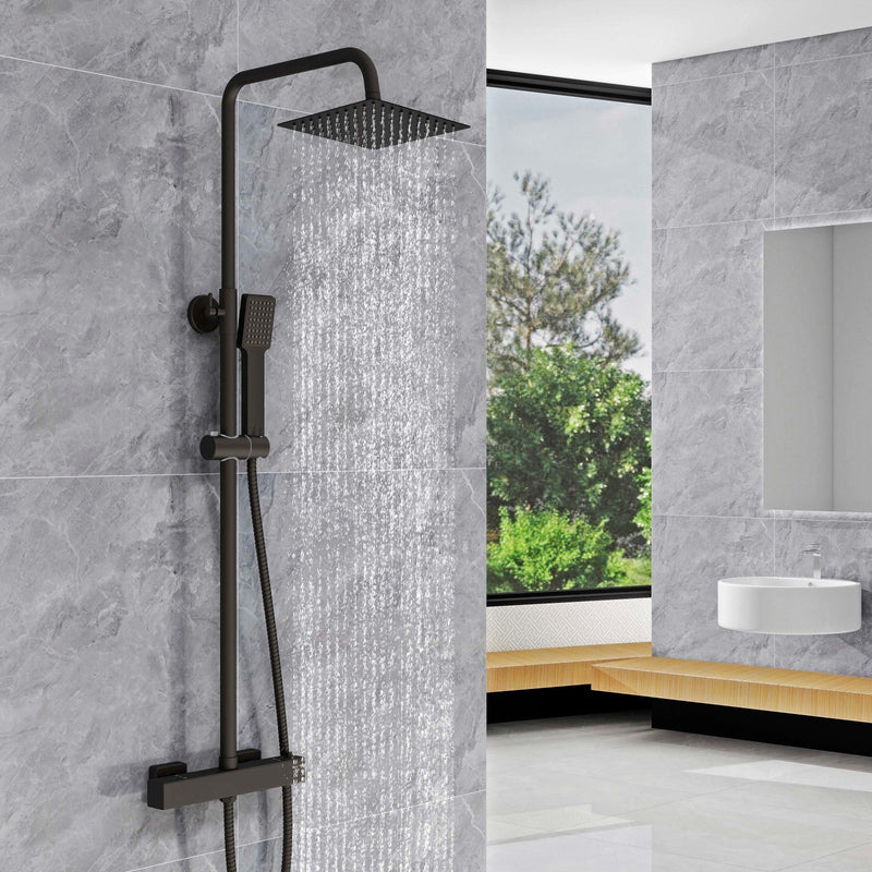 Black shower system mounted on a gray tiled wall with a bathroom setting in the background.